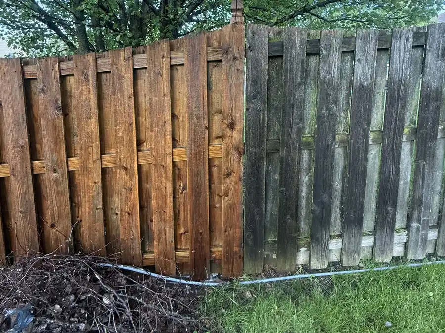 Wood privacy fence halfway through cleaning: left side restored to warm brown, right side grey