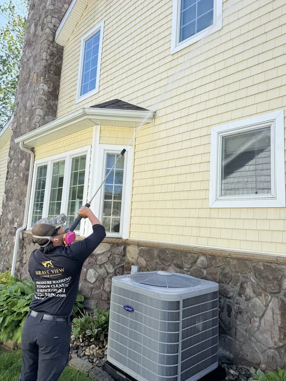 Brave View technician soft washing yellow siding on a Fort Wayne home with a long wand