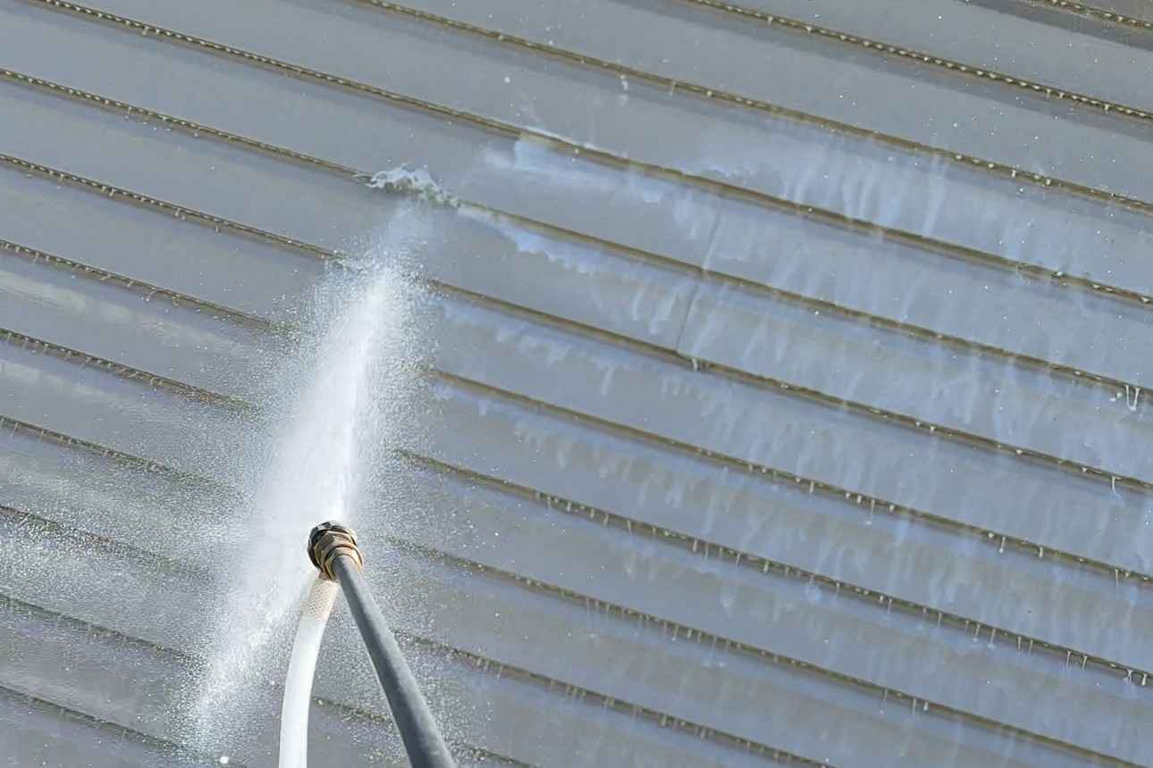 Spray wand soft washing grey vinyl siding with a fine fan of water