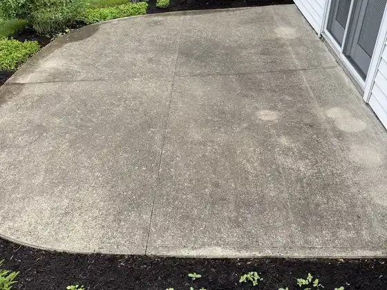 Before cleaning: grey concrete patio by a sliding door, marked with dark rings and grime
