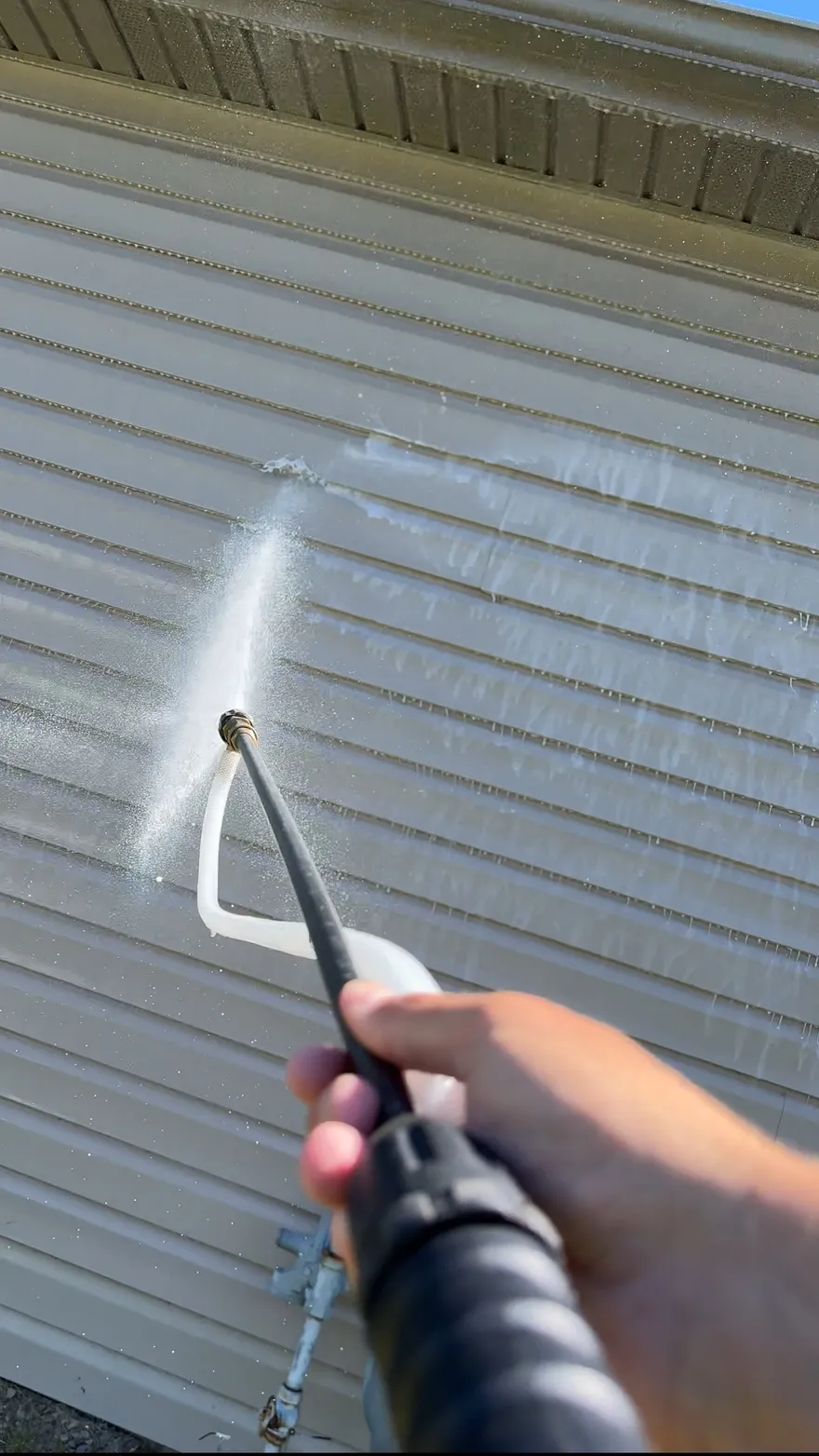Spray wand soft washing beige vinyl siding, rinsing a clean stripe across the boards