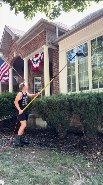 Window cleaner using a yellow water-fed pole on tall front windows of a brick home